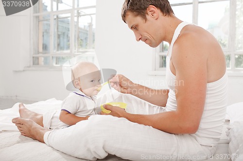 Image of Young father with his nine months old son on the bed at home