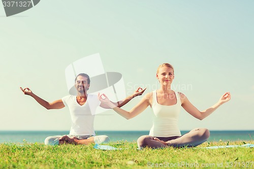 Image of smiling couple making yoga exercises outdoors