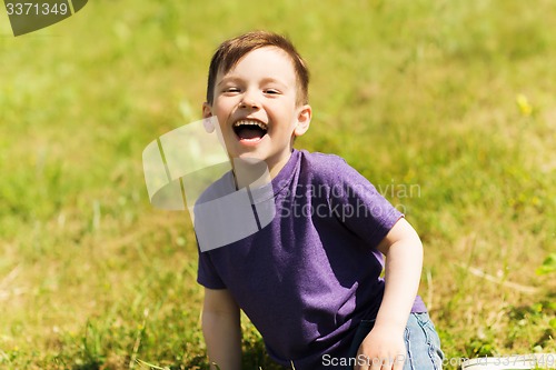 Image of happy little boy sitting on grass outdoors