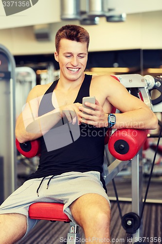 Image of smiling young man with smartphone in gym