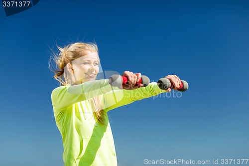Image of sporty woman with light dumbbells outdoors