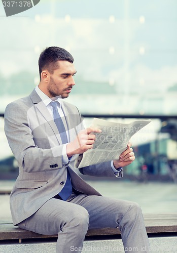 Image of young serious businessman newspaper outdoors