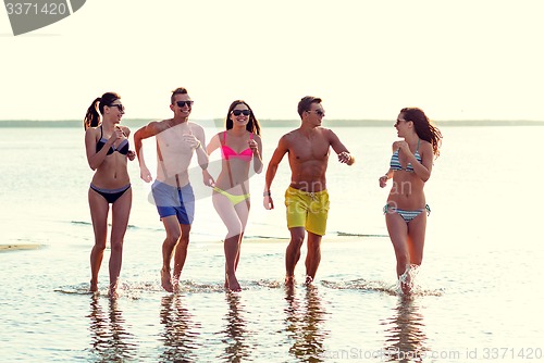 Image of smiling friends in sunglasses running on beach