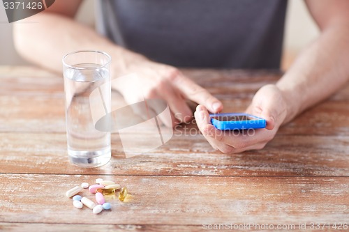 Image of close up of hands with smartphone, pills and water