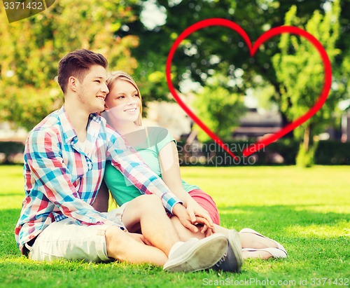 Image of smiling couple sitting on grass in summer park