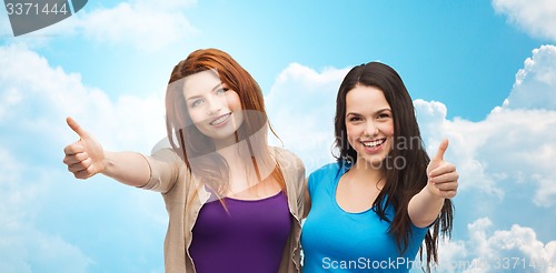Image of two smiling girls showing thumbs up over blue sky
