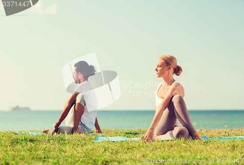 Image of smiling couple making yoga exercises outdoors