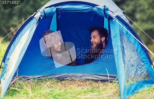 Image of smiling couple of tourists looking out from tent