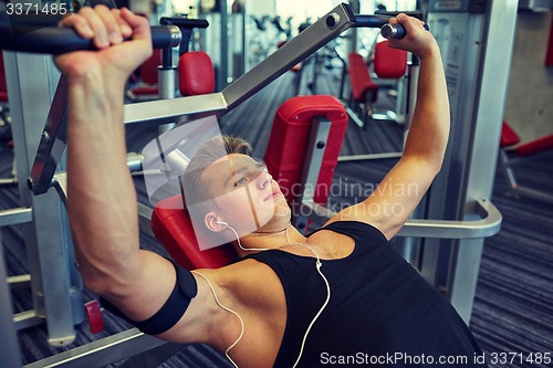 Image of young man with earphones exercising on gym machine