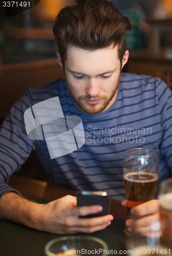 Image of man with smartphone drinking beer at bar