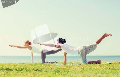 Image of smiling couple making yoga exercises outdoors