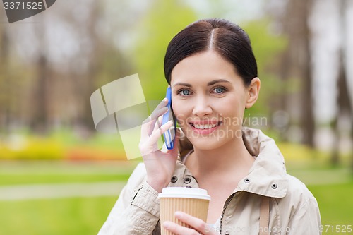 Image of smiling woman with smartphone and coffee in park