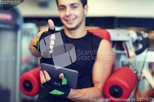 Image of young man with tablet pc showing thumbs up in gym