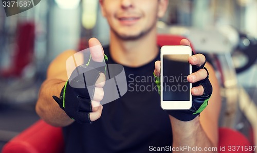 Image of young man with smartphone showing thumbs up in gym