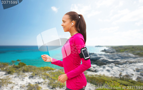 Image of happy woman with smartphone running on beach