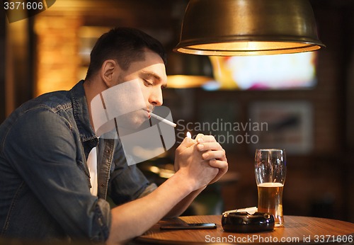 Image of man drinking beer and smoking cigarette at bar