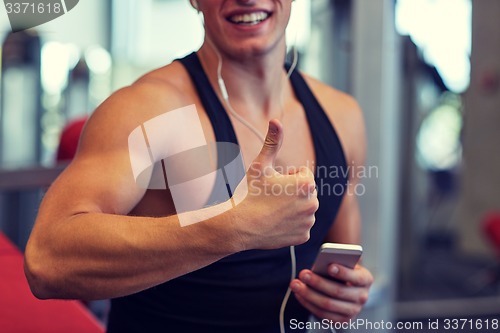 Image of happy man with smartphone and earphones in gym