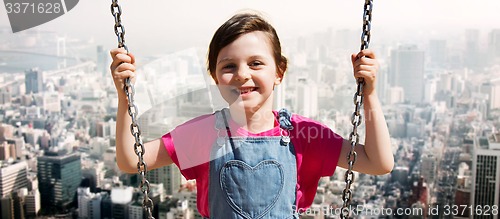 Image of happy little girl swinging on swing over city