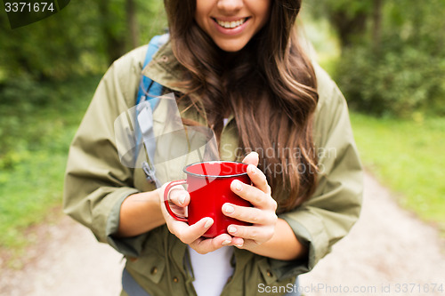 Image of smiling young woman with cup and backpack hiking