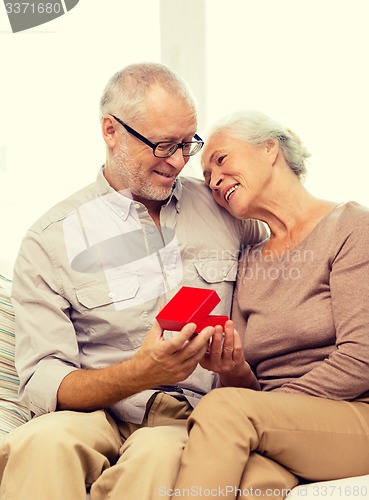 Image of happy senior couple with red gift box at home