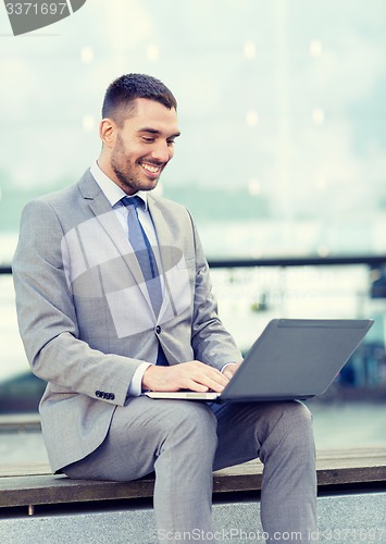 Image of smiling businessman working with laptop outdoors