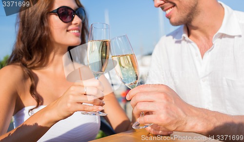 Image of smiling couple clinking champagne glasses at cafe