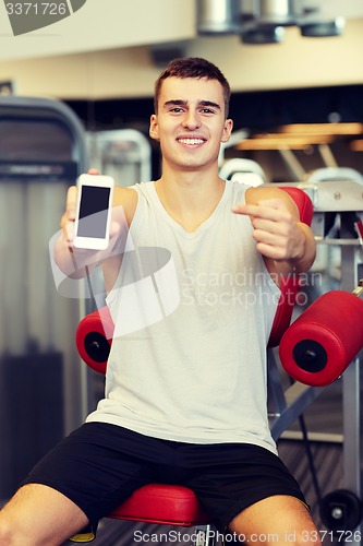 Image of smiling young man with smartphone in gym