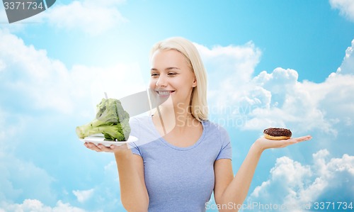 Image of smiling woman with broccoli and donut over sky