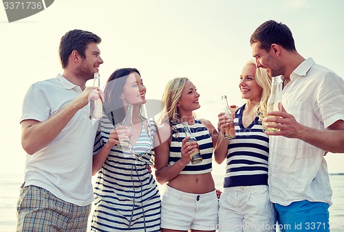 Image of smiling friends with drinks in bottles on beach