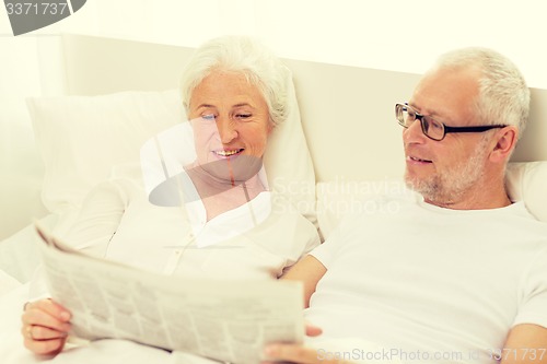 Image of happy senior couple with newspaper in bed