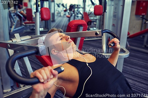 Image of young man with earphones exercising on gym machine