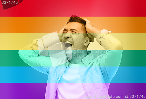 Image of unhappy gay man shouting over rainbow flag