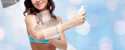 Image of happy young woman in swimsuit applying sunscreen