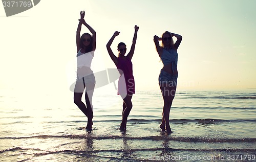 Image of happy female friends dancing on beach