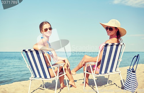 Image of happy women sunbathing in lounges on beach