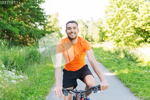 Image of happy young man riding bicycle outdoors