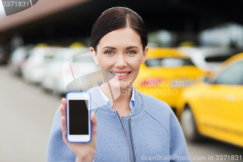 Image of smiling woman showing smartphone over taxi in city