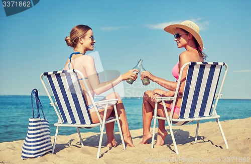 Image of happy women clinking bottles and drinking on beach