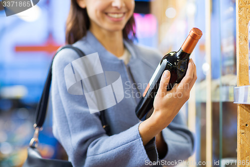 Image of happy woman choosing and buying wine in market