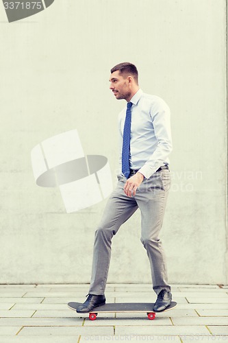 Image of young smiling businessman with skateboard outdoors