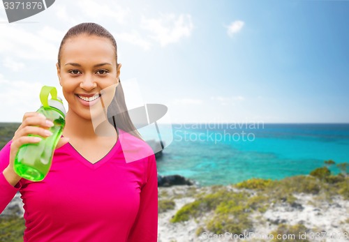 Image of happy african woman drinking from bottle outdoors