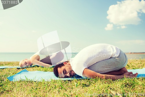 Image of smiling couple making yoga exercises outdoors