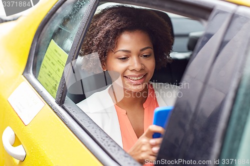 Image of happy african woman texing on smartphone in taxi