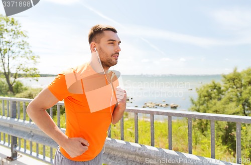 Image of happy man with earphones running outdoors