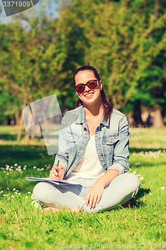 Image of smiling young girl with notebook writing in park