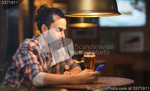 Image of man with smartphone and beer texting at bar