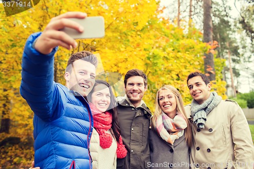 Image of smiling friends with smartphone in city park