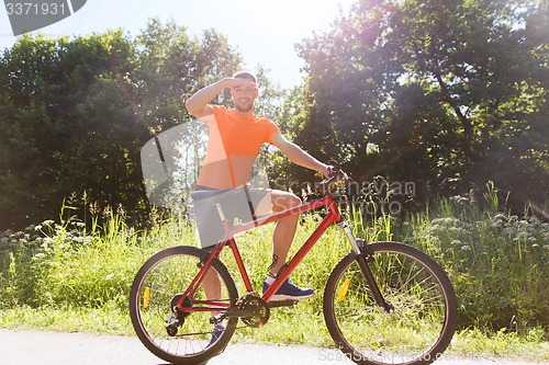 Image of happy young man riding bicycle outdoors