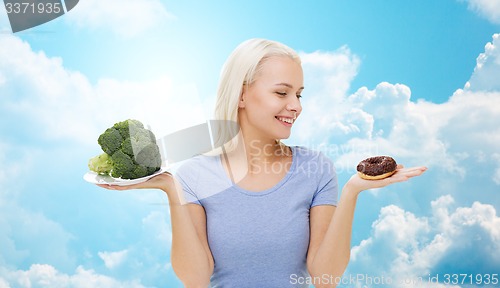 Image of smiling woman with broccoli and donut over sky