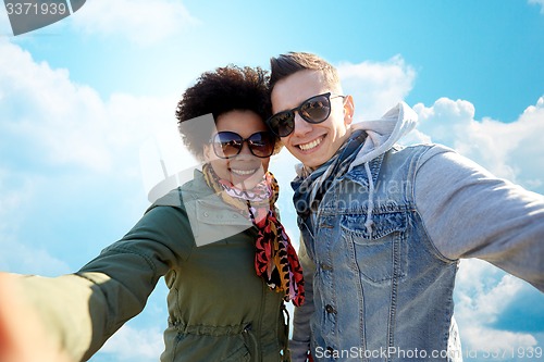Image of happy teenage couple taking selfie over blue sky